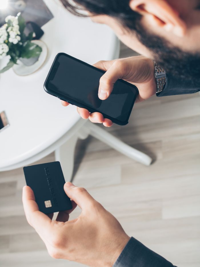 Un homme utilisant un smartphone et une carte bancaire pour un paiement en ligne, illustrant les concepts de finance numérique.